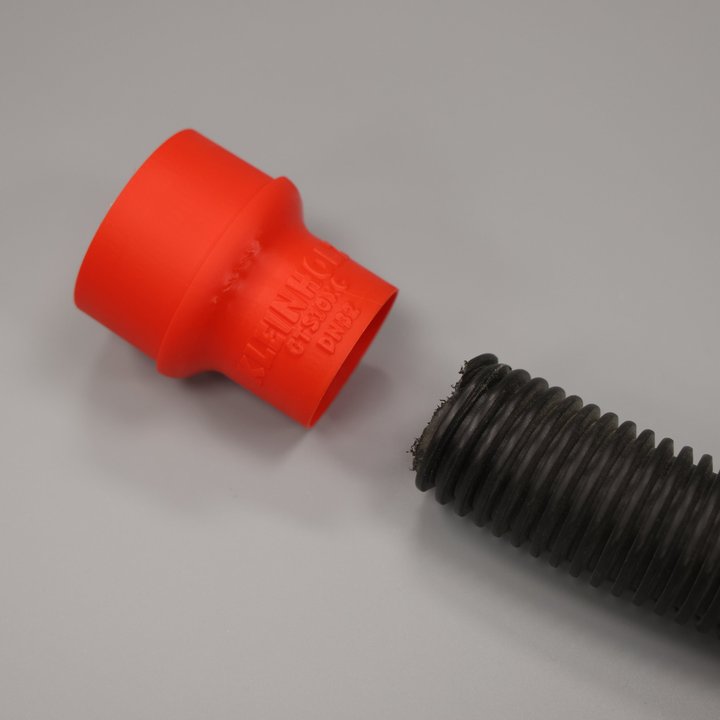 Roter Adapter DN32 neben einem schwarzen Wellschlauch